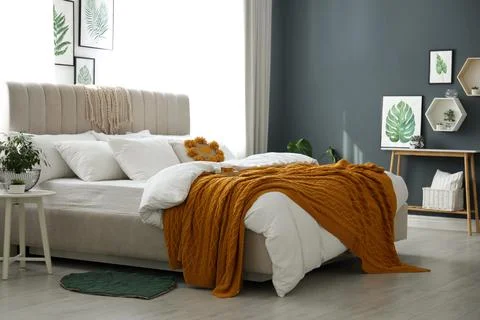 Comfortable bed with knitted orange plaid in stylish room interior Stock Photos