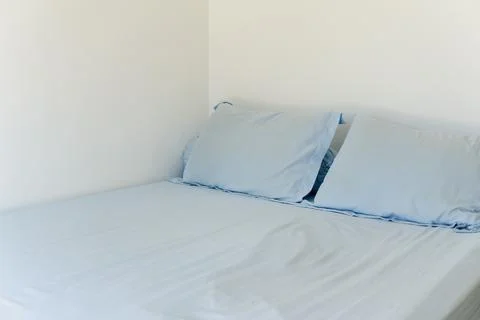 A comfortable bed with light blue bedding and pillows in a minimalist bedro.. 写真素材
