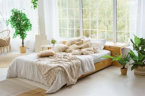 Comfortable bed with lots of soft decorative beige pillows in light sunny b.. Stock Photos