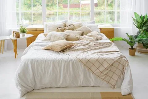 Comfortable bed with lots of soft decorative beige pillows in light sunny b.. Stock Photos