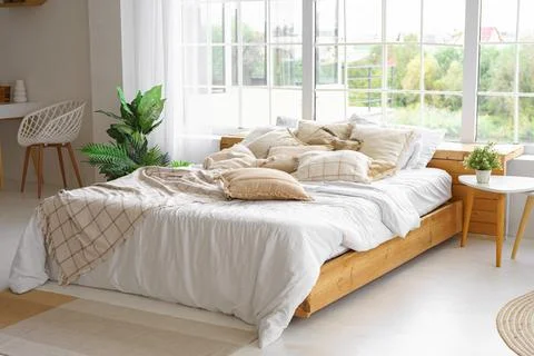 Comfortable bed with lots of soft decorative beige pillows in light sunny b.. Stock Photos
