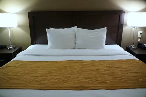 A comfortable bed with white pillows, bed sheet and mustard blanket Stock Photos