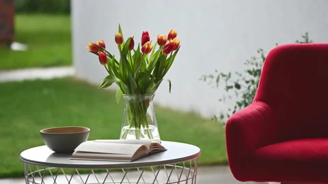 Comfortable chair , little table with book and vase of tulips on modern terra Stock Footage 199501074