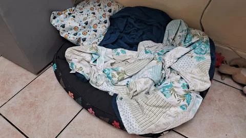 Comfortable dog bed featuring soft patterned blankets on tiled floor surface Stock Photos