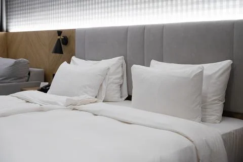 A comfortable hotel bed with crisp white pillows and bedding against a grey Stock Photos