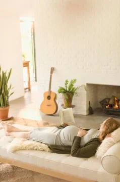 Comfortable pregnant woman laying reading book near fireplace in living room Stock Photos