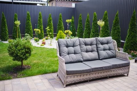 Comfortable wicker sofa with grey cushions in a modern landscaped Stock Photos