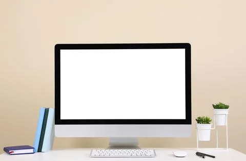 Comfortable workplace with blank computer display on desk near beige wall. Sp Stock Photos