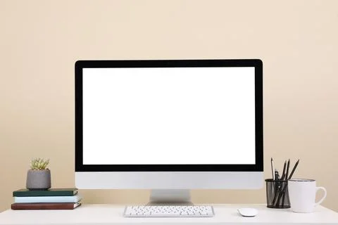 Comfortable workplace with blank computer display on desk near beige wall. Sp Stock Photos