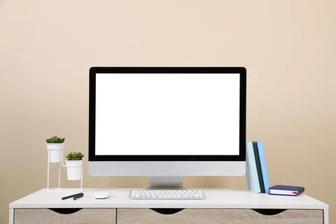 Comfortable workplace with blank computer display on desk near beige wall. Sp Stock Photos