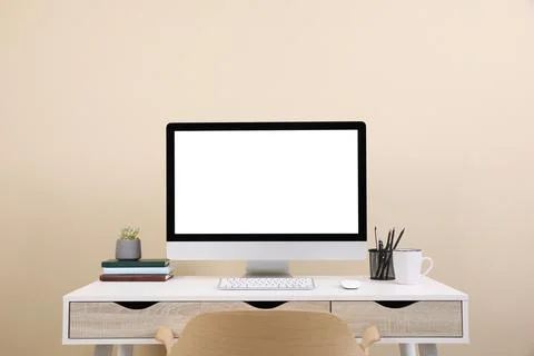 Comfortable workplace with blank computer display on desk near beige wall. Sp Stock Photos