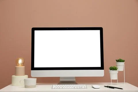 Comfortable workplace with blank computer display on desk near light brown wa Stock Photos