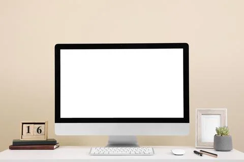 Comfortable workplace with blank computer display on desk near beige wall. Sp Stock Photos