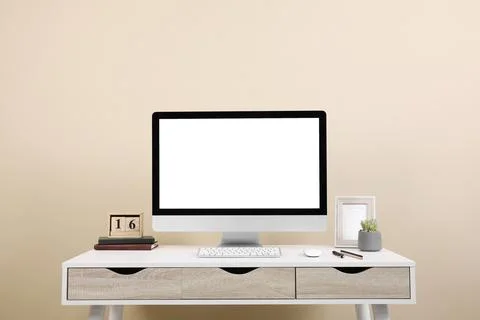 Comfortable workplace with blank computer display on desk near beige wall. Sp Stock Photos