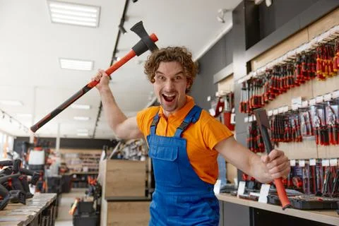 Comic crazy salesman attacking with to axes standing over hardware store Foto stock