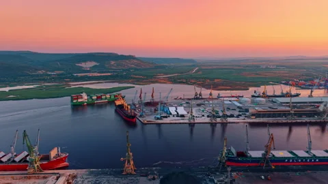 Commercial cargo port at sunset. Large container ships dock near cranes along a Stock Footage 342573199