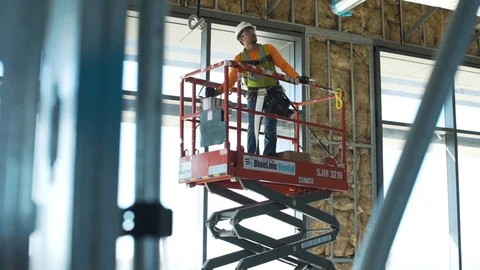 Commercial Construction worker raises and maneuvers man lift to work on Stock Footage 104875277