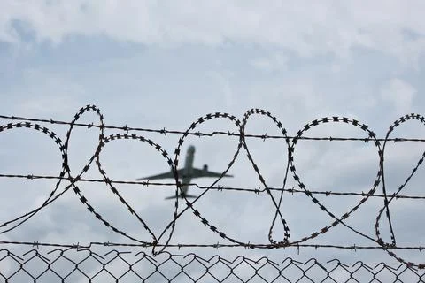 Commercial Jet Airliner Climbing in Cloudy Sky Beyond Barbed Wire Fence Stock Photos