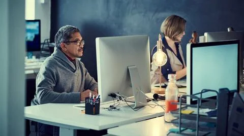 Committed to accomplishing their deadlines. two businesspeople working late in Stock Photos
