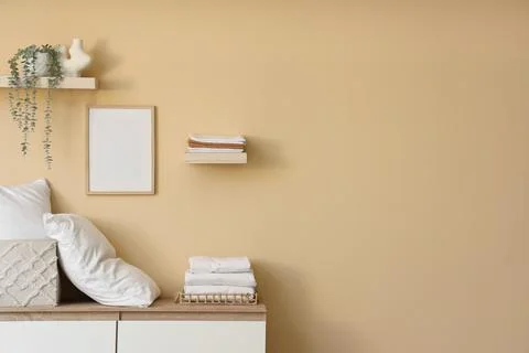 Commode with shelves, stack of clean bed sheets and pillows near beige wall i Stock Photos
