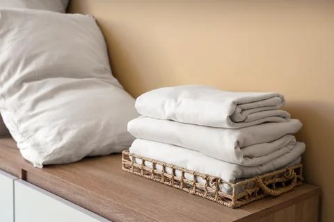 Commode with stack of clean bed sheets and pillow near beige wall in living r Stock Photos