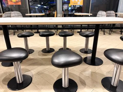 A communal high table with a row of modern, black leather or vinyl stools Stock Photos