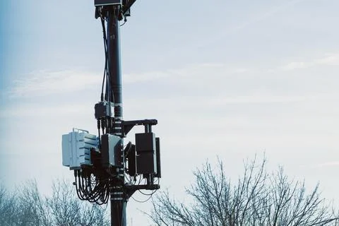 Communication technology is shown on a tower against the sky with trees in .. Fotos Stock