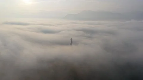 Communication tower peeking through dense fog with mountain backdrop at dawn 스톡 동영상 345504964