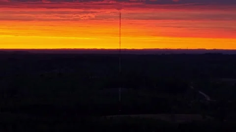 Communication tower silhouetted against a dramatic sunrise over a dark forest Stock Footage 340861047