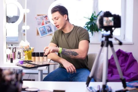 Communicative interested man having different makeup products on the table Stock Photos