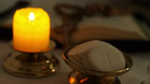 Communion hosts in twilight illuminated by the light of a lit candle rosary Vídeo Stock 136473992