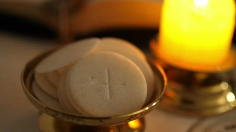 Communion hosts in twilight illuminated by the light of a lit candle Vídeo Stock 136474007