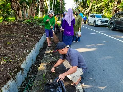 Community activities are pulling out grass on the side of the road and in ditche Fotos de archivo