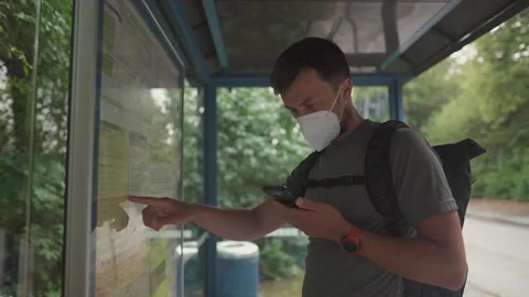 Commuter with backpack and smartphone reading route schedule and transit map at Stock Footage 328234764