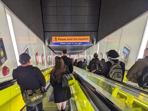 Commuters riding down the long, modern escalator at Canary Wharf station in East Foto stock