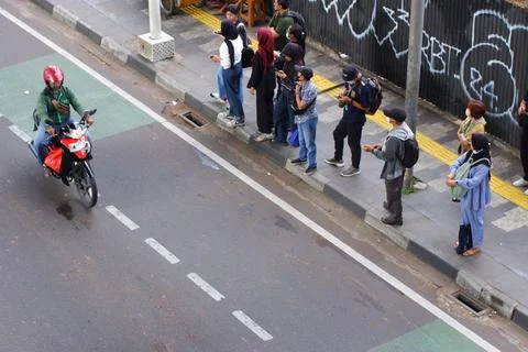 Commuters Using Phones While Waiting for Transport on Jakarta Sidewalk Stock Photos