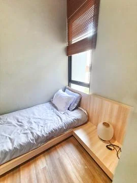 A compact bedroom with a single bed dressed in a light gray comforter and whi Stock Photos