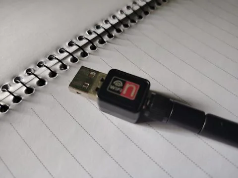 Compact black USB WiFi adapter with antenna resting on a lined notebook pag.. Fotos Stock