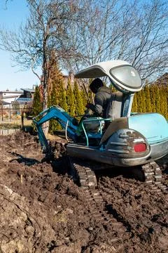 Compact blue mini excavator digs wet soil in suburban garden Stock-Fotos