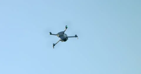 Compact camera drone banking in flight against a clear blue sky, propellers Stock Footage 343927999