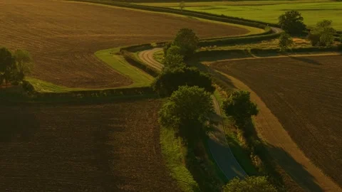 Compact car driving along winding country road surrounded by sunset fields. Stock Footage 328358458