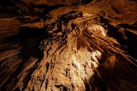 Compact cluster of stalactites and amber limestone deposits illuminated ben.. Stock Photos
