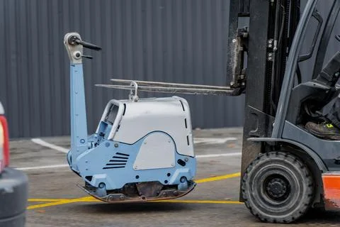 Compact construction compactor lifted by forklift on concrete surface Stock Photos