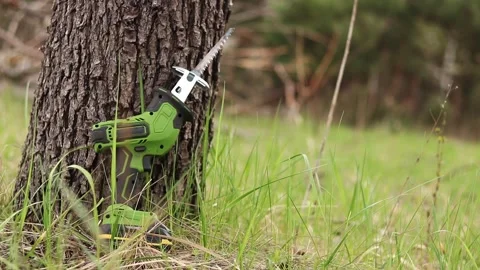 Compact cordless reciprocating saw leaning against a tree trunk Stock Footage 333245795