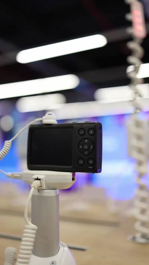 Compact digital camera displayed on security stand in an electronics store Stock Footage 345357504