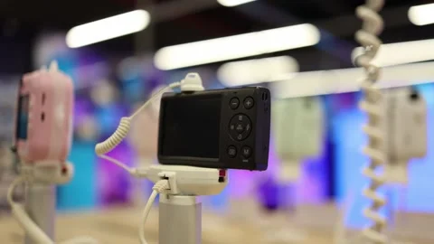 Compact digital camera secured on display stand inside electronics store Stock Footage 345359184