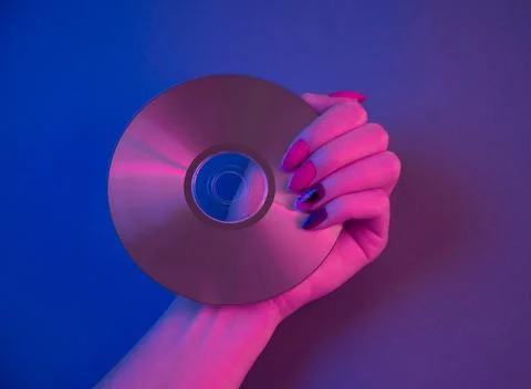Compact disc in purple neon light and female hand with retrowave manicure. Stock Photos