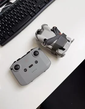 Compact drone and remote controller on a white desk near a computer keyboar.. Stock Photos