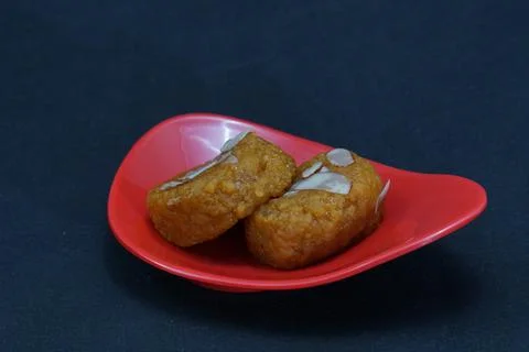 A compact, elegantly designed red dish contains two pieces of Mohanthal, a .. Stock Photos