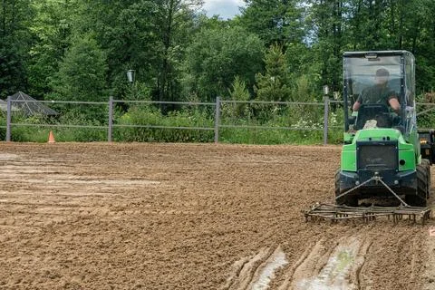 Compact green mini loader tractor levelling sand soil with drag harrow harr.. Stock Photos